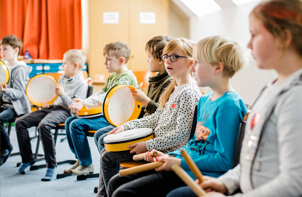Grundschulkinder musizieren mit Tambourins und Klanghölzern